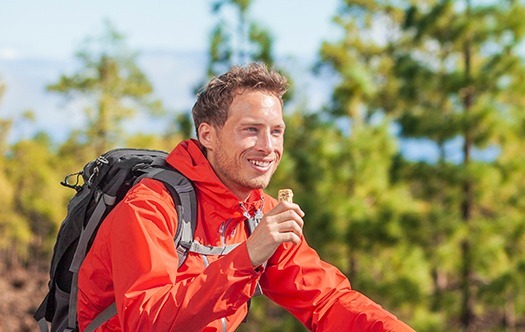Müsliriegel-Snack auf Waldwanderung essen Glücklicher Camper-Mann, der in der Naturlandschaft wandert und gesundes Essen hält